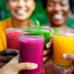 Women toasting with smoothies, with lush greenery in the background